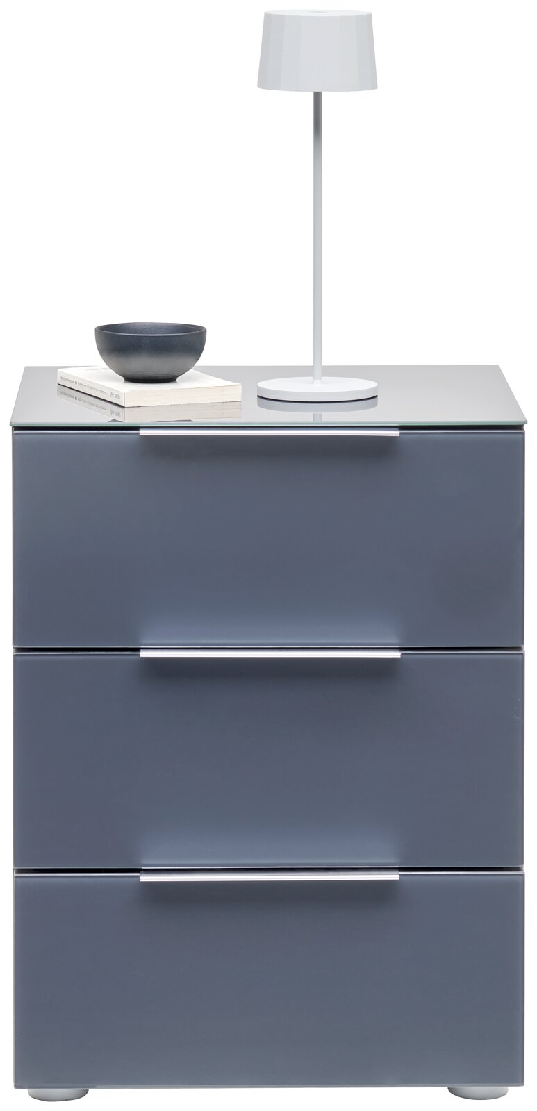 Moderne Nachtkonsole mit drei Schubladen in grauer Farbe, darauf eine weiße Tischlampe, eine Schale und Bücher. Frontalansicht.