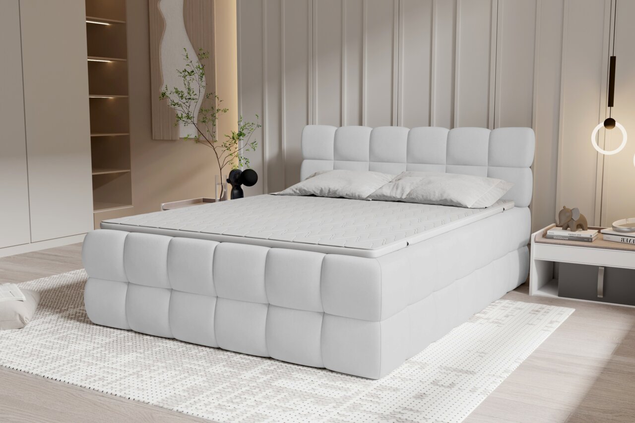 Modernes, weiß gepolstertes Polsterbett mit quadratisch gestepptem Kopf- und Fußteil in einem hellen Schlafzimmer, gezeigt in schräger Frontansicht von links.