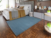 Blauer Uni-Teppich im Schlafzimmer, von der Seite betrachtet, auf einem Holzboden neben einem modernen Bett und einer Kommode.