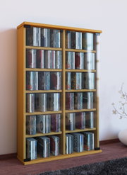 Holzfarbenes CD-Regal mit transparenter Front und mehreren Fächern, gefüllt mit CDs, freistehend im Wohnraum – Perspektive: leicht schräg von vorne (3/4-Ansicht).
