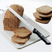 Brotmesser CLASSIC LINE 21cm mit schwarzem Griff, auf einem Schneidebrett mit geschnittenem Brot, seitliche Perspektive