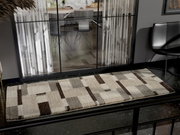 Moderner Teppich in rechteckiger Form mit geometrischem Muster in Beige- und Brauntönen, auf dunklem Boden vor einer Glaswand mit Blick in einen Essbereich.