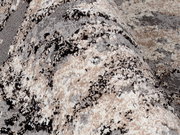 Nahaufnahme eines strukturierten Teppichs in Beige-, Grau- und Schwarztönen, perspektivisch von der Seite aufgenommen.