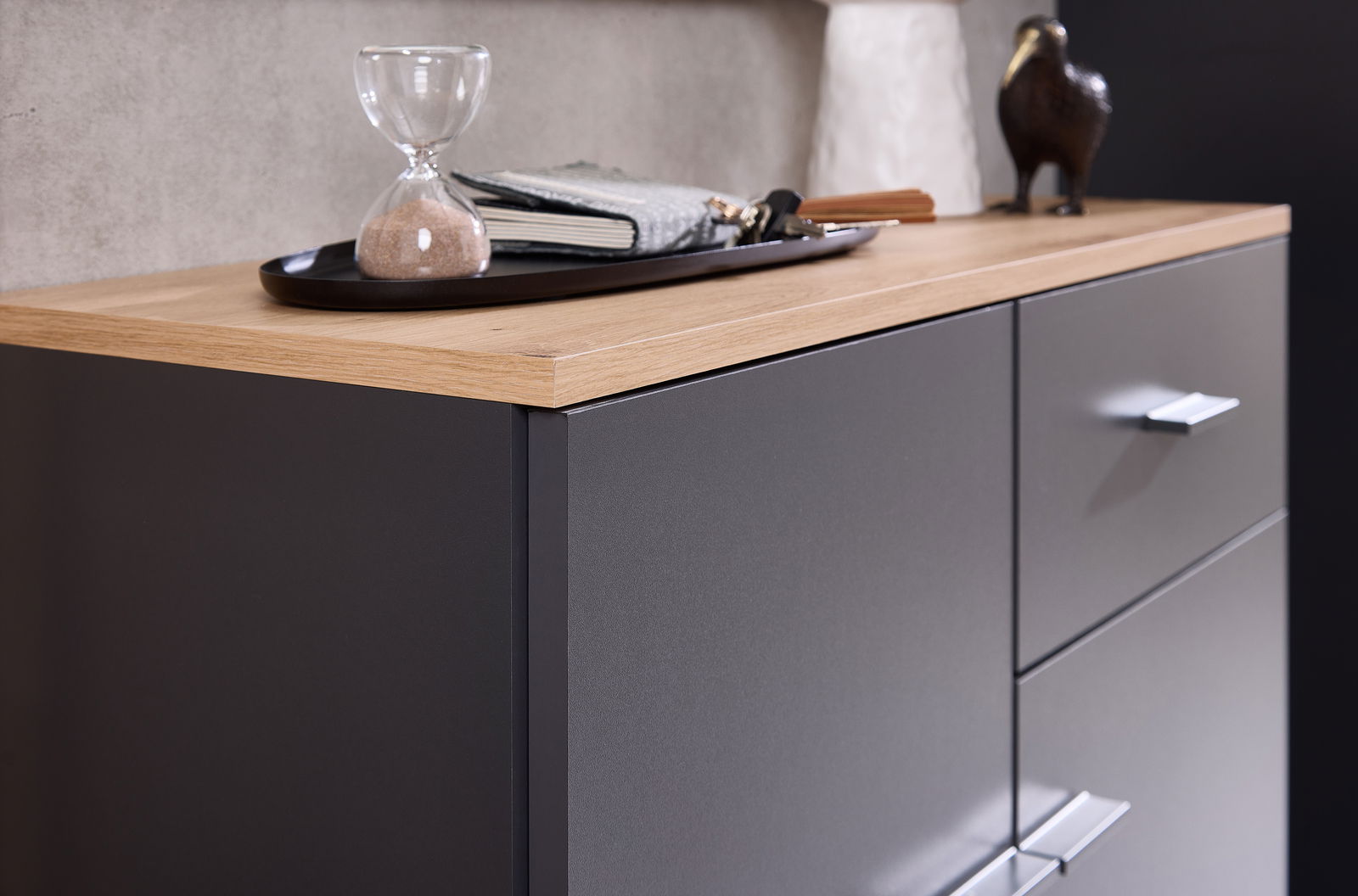 Nahaufnahme einer Kompaktgarderobe mit dunkler Oberfläche und heller Holzplatte, darauf eine Sanduhr und Dekorationen.