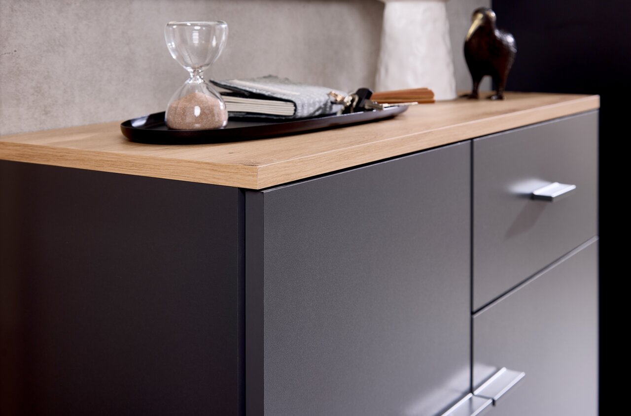 Nahaufnahme einer Kompaktgarderobe mit dunkler Oberfläche und heller Holzplatte, darauf eine Sanduhr und Dekorationen.