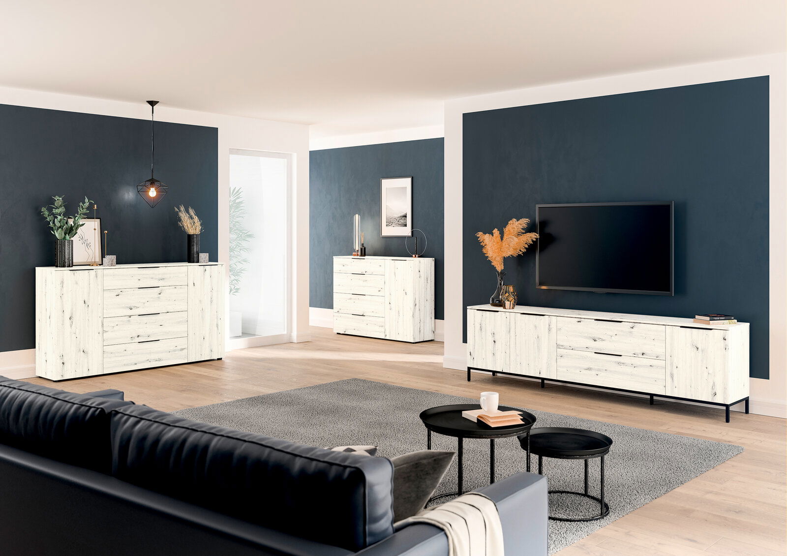 Moderne Wohnzimmermöbel in heller Holzoptik, bestehend aus einem TV-Lowboard, einer Kombikommode und einer Schubkastenkommode, in einem stilvoll eingerichteten Raum mit dunklen Wänden und Holzboden. Perspektive von der Seite.