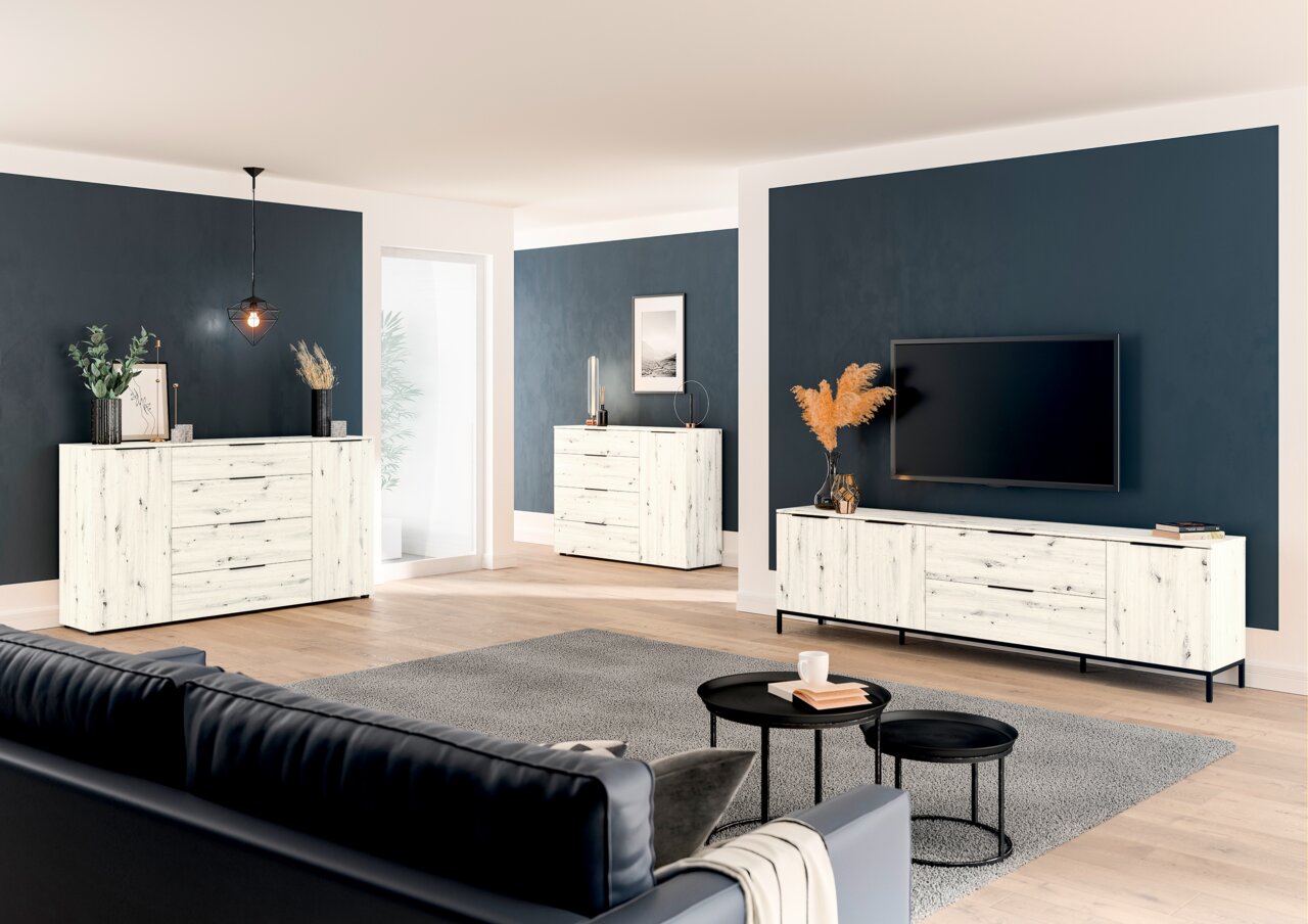 Moderne woonkamermeubels in een lichte houtlook, bestaande uit een tv-lowboard, een gecombineerde ladekast en een ladekast, in een stijlvol ingerichte ruimte met donkere muren en een houten vloer. Zijaanzicht.