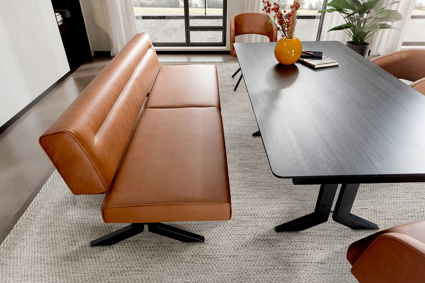 Moderne Esszimmer-Sitzbank in braunem Leder mit schwarzem Metallgestell, neben einem dunklen Esstisch, aus der Vogelperspektive fotografiert.