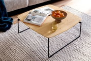 Vierkante salontafel met licht houten blad en zwart metalen frame in een woonkamer, met open boek, fruitschaal met sinaasappels en glas; schuin van boven gefotografeerd.
