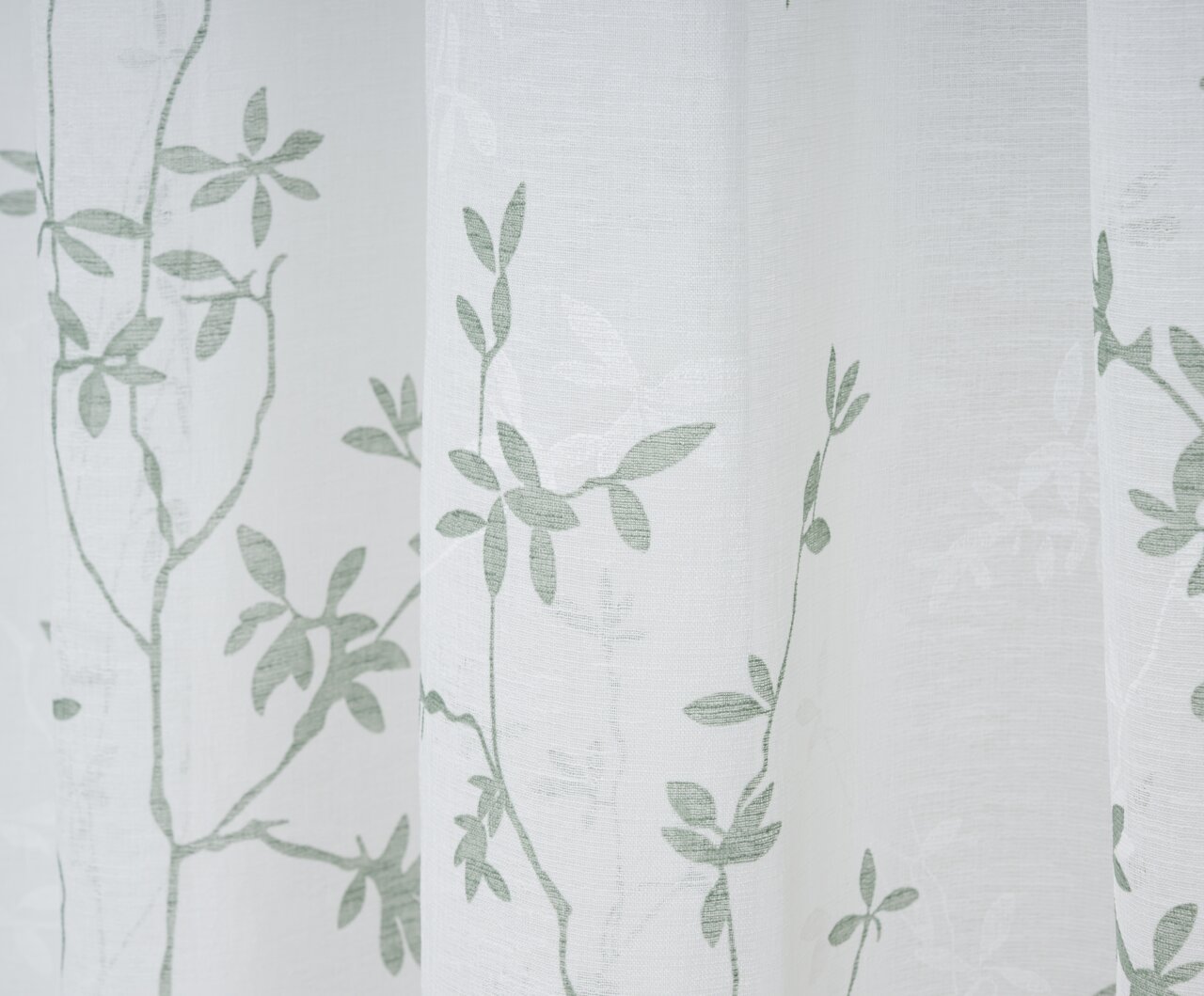 Nahaufnahme eines weißen Vorhangs mit grünem Blattmuster, fotografiert aus seitlicher Perspektive.