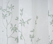 Nahaufnahme eines weißen Vorhangs mit grünem Blattmuster, fotografiert aus seitlicher Perspektive.