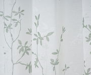 Nahaufnahme eines weißen Vorhangs mit grünem Blattmuster, fotografiert aus seitlicher Perspektive.