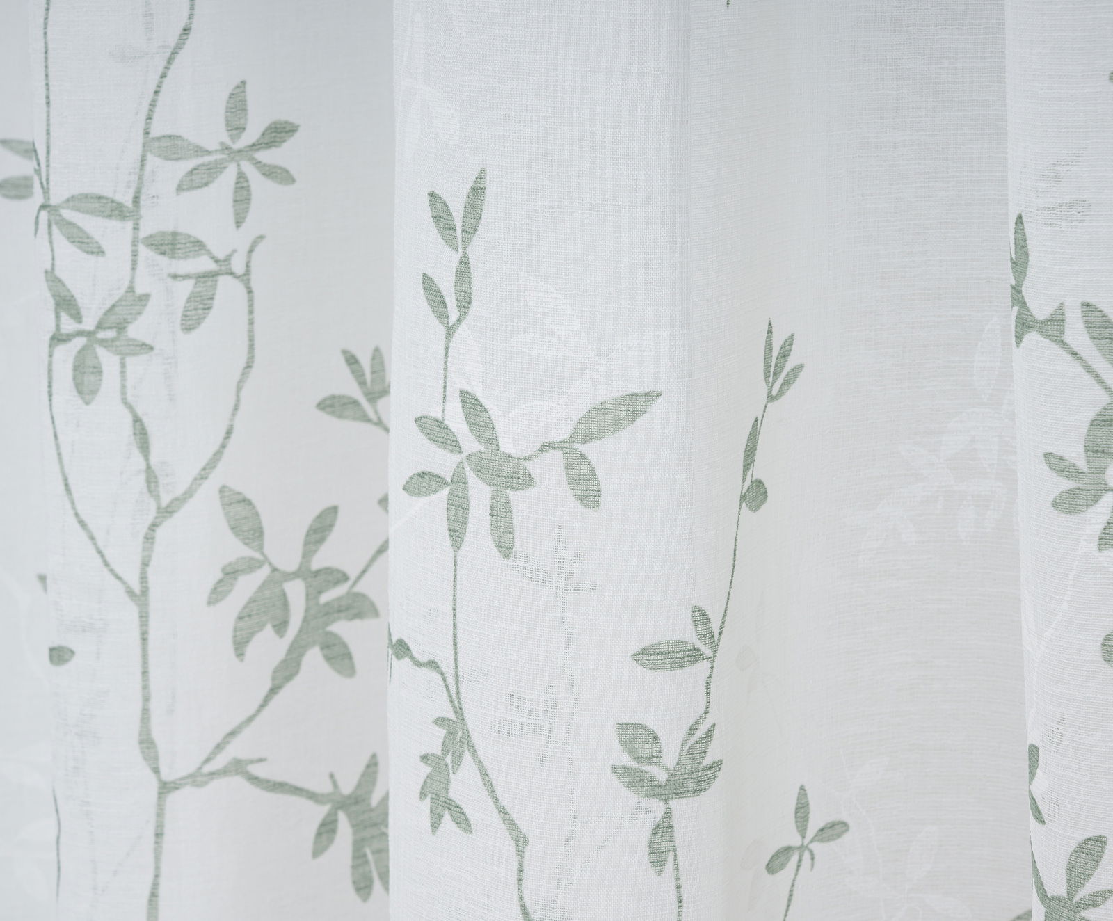 Nahaufnahme eines weißen Vorhangs mit grünem Blattmuster, fotografiert aus seitlicher Perspektive.