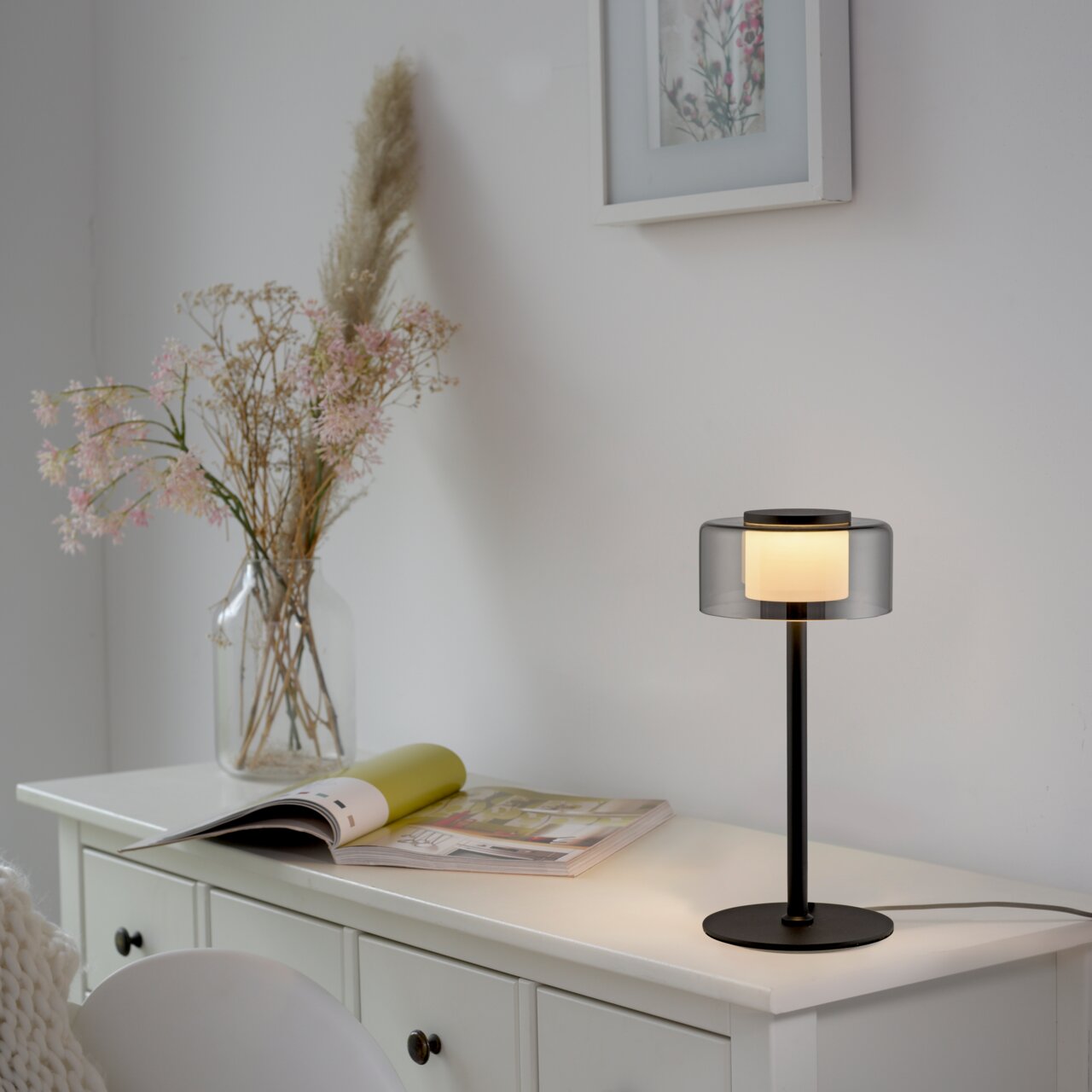 Paul Neuhaus Tischleuchte RIKA Moderne Tischleuchte RIKA mit schwarzem Standfuß und transparentem Lampenschirm, seitliche Perspektive auf einem weißen Schrank platziert.