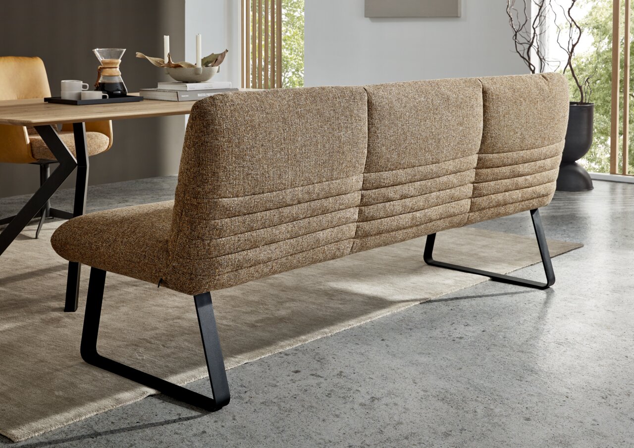 Achterkant van een moderne bank met bruine stoffen bekleding en zwarte metalen poten in een eetkamer.