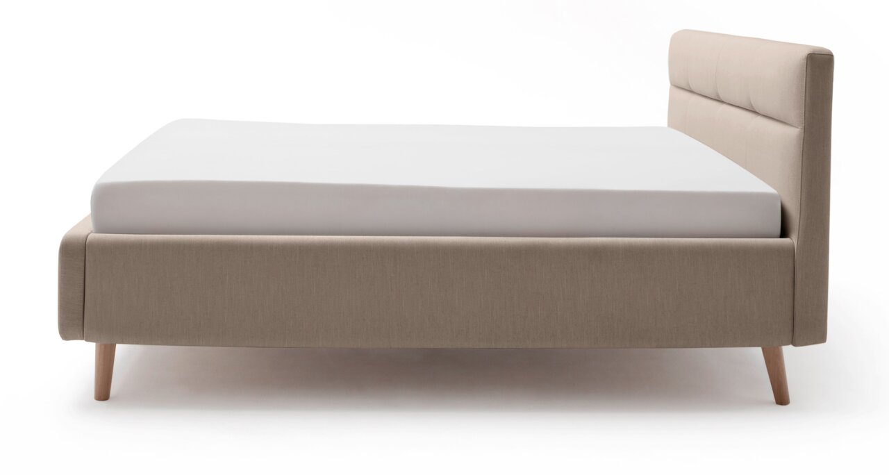 Zijaanzicht van een modern gestoffeerd bed in beige met houten poten en een gestoffeerd hoofdeinde.