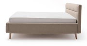 Zijaanzicht van een modern gestoffeerd bed in beige met houten poten en een gestoffeerd hoofdeinde.
