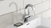 Moderne Waschtischarmatur aus Chrom in seitlicher Perspektive, montiert auf einem weißen Waschbecken mit Seifenschale.