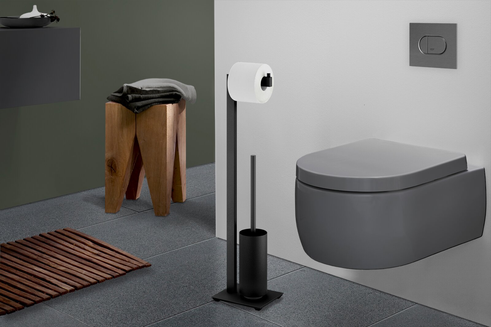 Modernes Badezimmer mit wandhängendem WC in Dunkelgrau, schwarzem freistehendem Toilettenpapierhalter mit Rollenhalter und WC-Bürste; Ansicht schräg von vorne rechts.