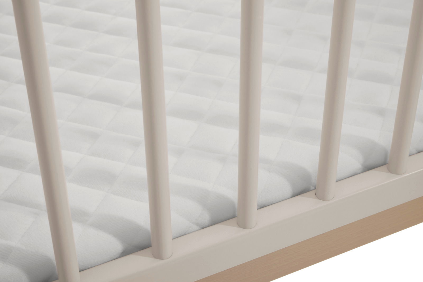 Nahaufnahme eines Anstellbetts mit weißen Gitterstäben und einer weißen, gesteppten Matratze, Perspektive von oben.