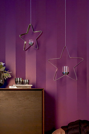 Zwei hängende sternförmige Teelichthalter aus Metall vor einer lila Wand, mit Kerzenhaltern in der Mitte. Perspektive: Frontalansicht.