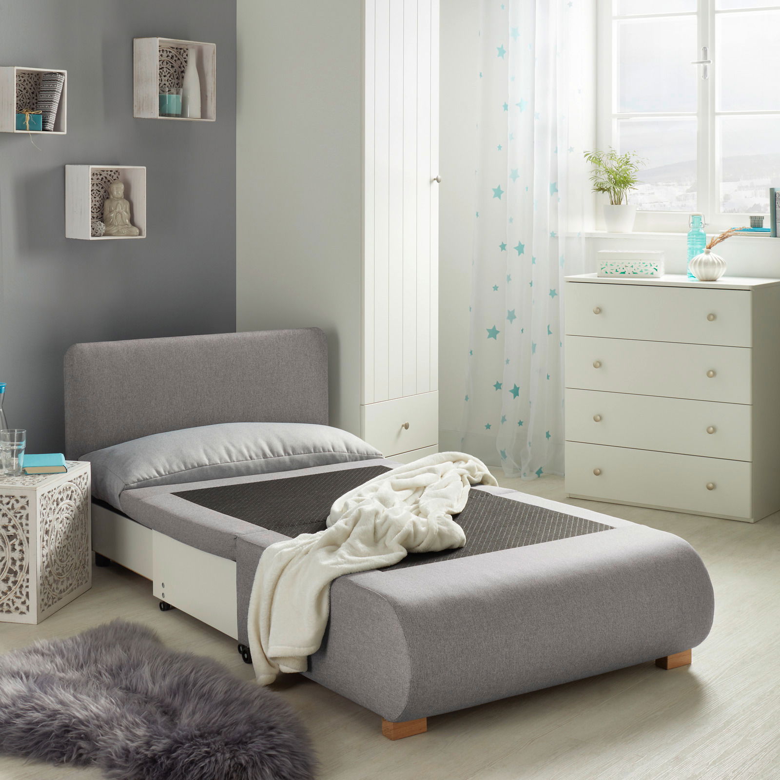 Grauer Funktionssessel in einem modernen Schlafzimmer, von der Seite betrachtet, mit ausgezogener Liegefläche und dekorativen Elementen im Hintergrund.