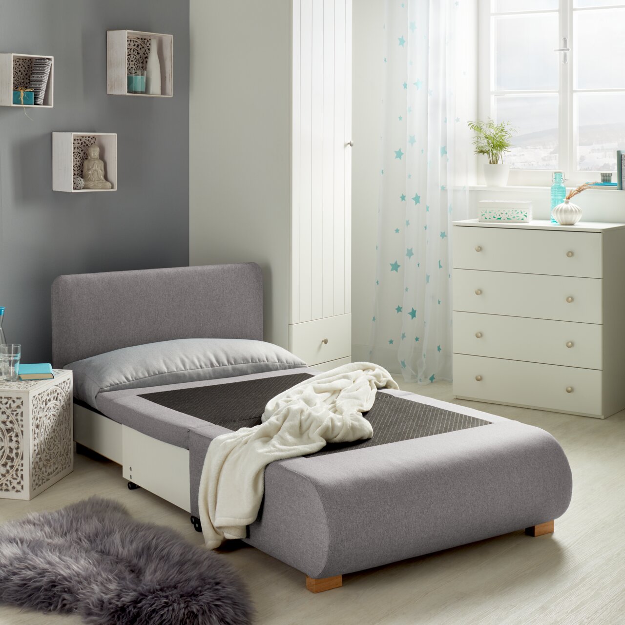 Grauer Funktionssessel in einem modernen Schlafzimmer, von der Seite betrachtet, mit ausgezogener Liegefläche und dekorativen Elementen im Hintergrund.