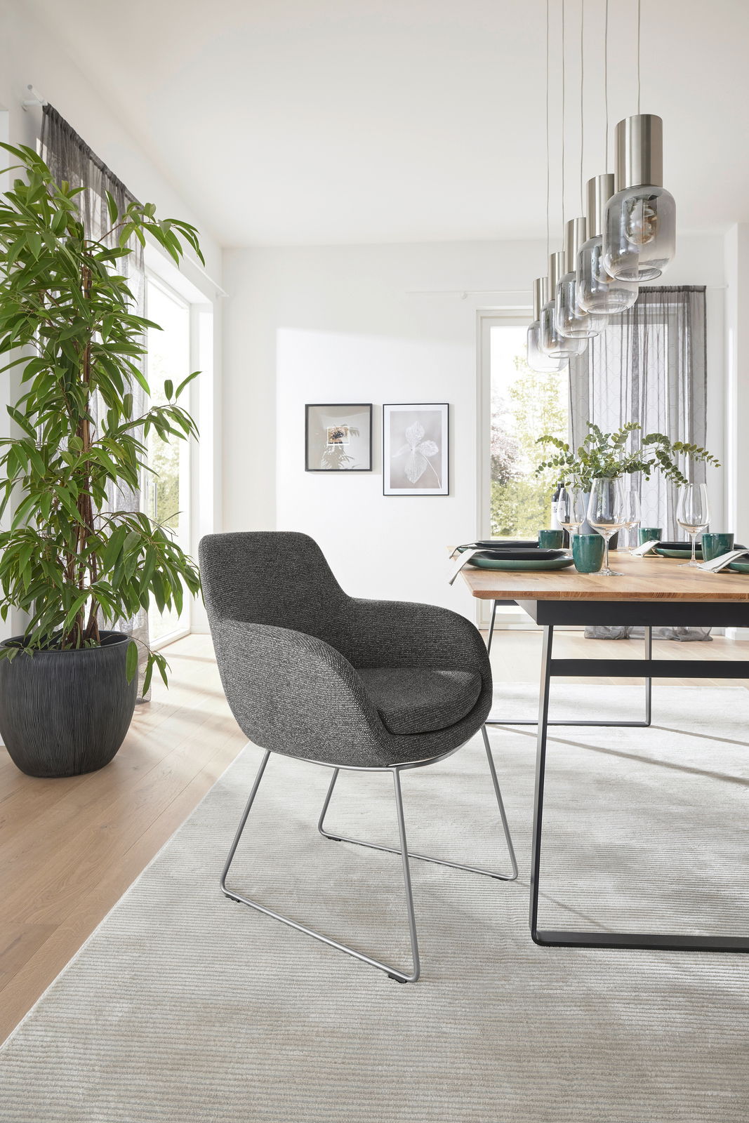 Musterring Armlehnstuhl MR TAVIA Grauer Armlehnstuhl mit modernem Design, seitliche Perspektive, in einem hellen Esszimmer mit Holztisch und Pflanzen.