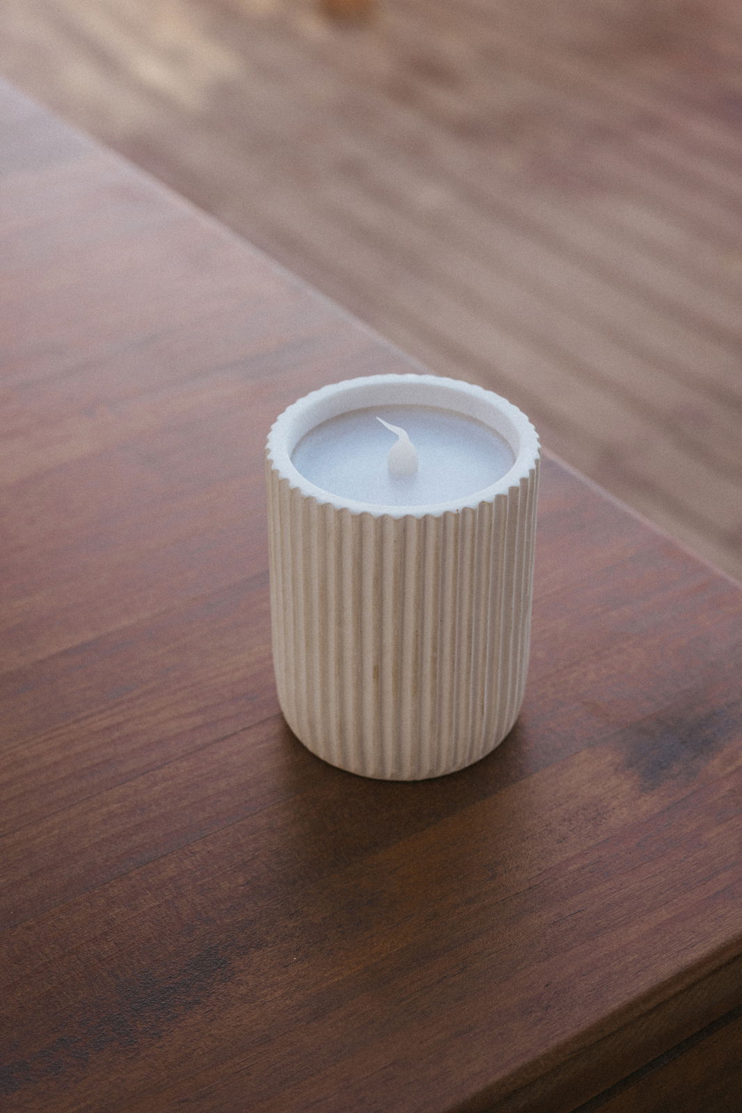 Outdoor-Kerze in einem geriffelten, weißen Behälter auf einem Holztisch aus der Vogelperspektive