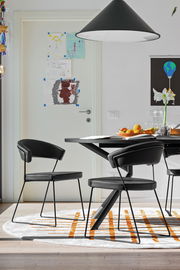 Moderner schwarzer Stuhl mit Metallbeinen, seitliche Perspektive, in einem Esszimmer mit Tisch und Dekorationen.