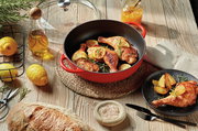 Rote Bauernpfanne Provence 28cm mit gebratenem Hähnchen und Zitronenscheiben, von oben fotografiert, umgeben von frischen Zutaten wie Zitronen, Olivenöl und Brot auf einem Holztisch.