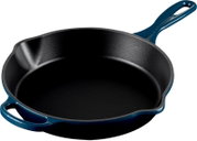 Gietijzeren koekenpan met donkerblauwe geëmailleerde buitenkant, zwarte binnenkant en twee handgrepen, schuin van boven gefotografeerd op witte achtergrond
