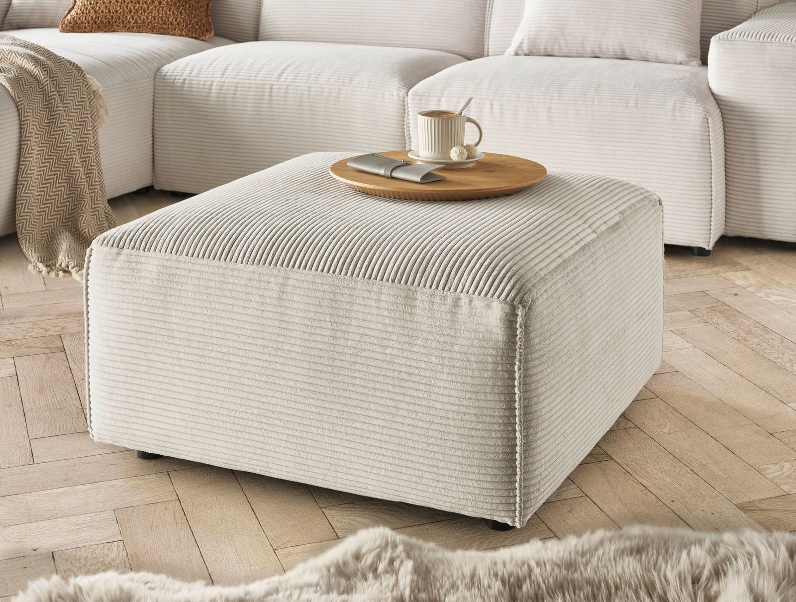 Beiger Hocker in einem Wohnzimmer, aus einer leicht erhöhten Perspektive fotografiert, mit einer Tasse und einem Teller darauf.