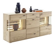 Modernes Sideboard aus hellem Holz mit dekorativen Vasen und Büchern auf der Oberseite, seitliche Glasvitrinen mit Beleuchtung, Perspektive von vorne links.