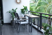 Moderner Beistelltisch auf einem Balkon, umgeben von Pflanzen, mit zwei Stühlen und einer Tasse Kaffee, seitliche Perspektive.