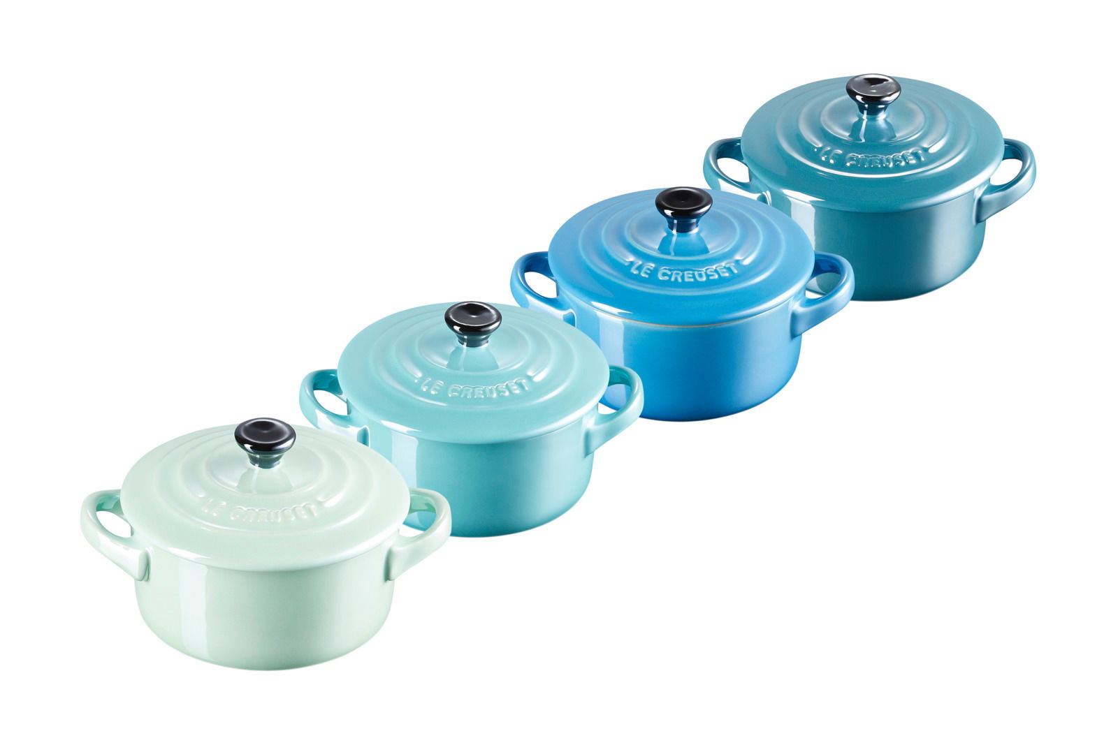 LE CREUSET Mini-Cocotte 4er-Set 10cm Metallics Blau-Grün Vier Mini Cocottes in verschiedenen Blau- und Grüntönen, von schräg oben fotografiert.