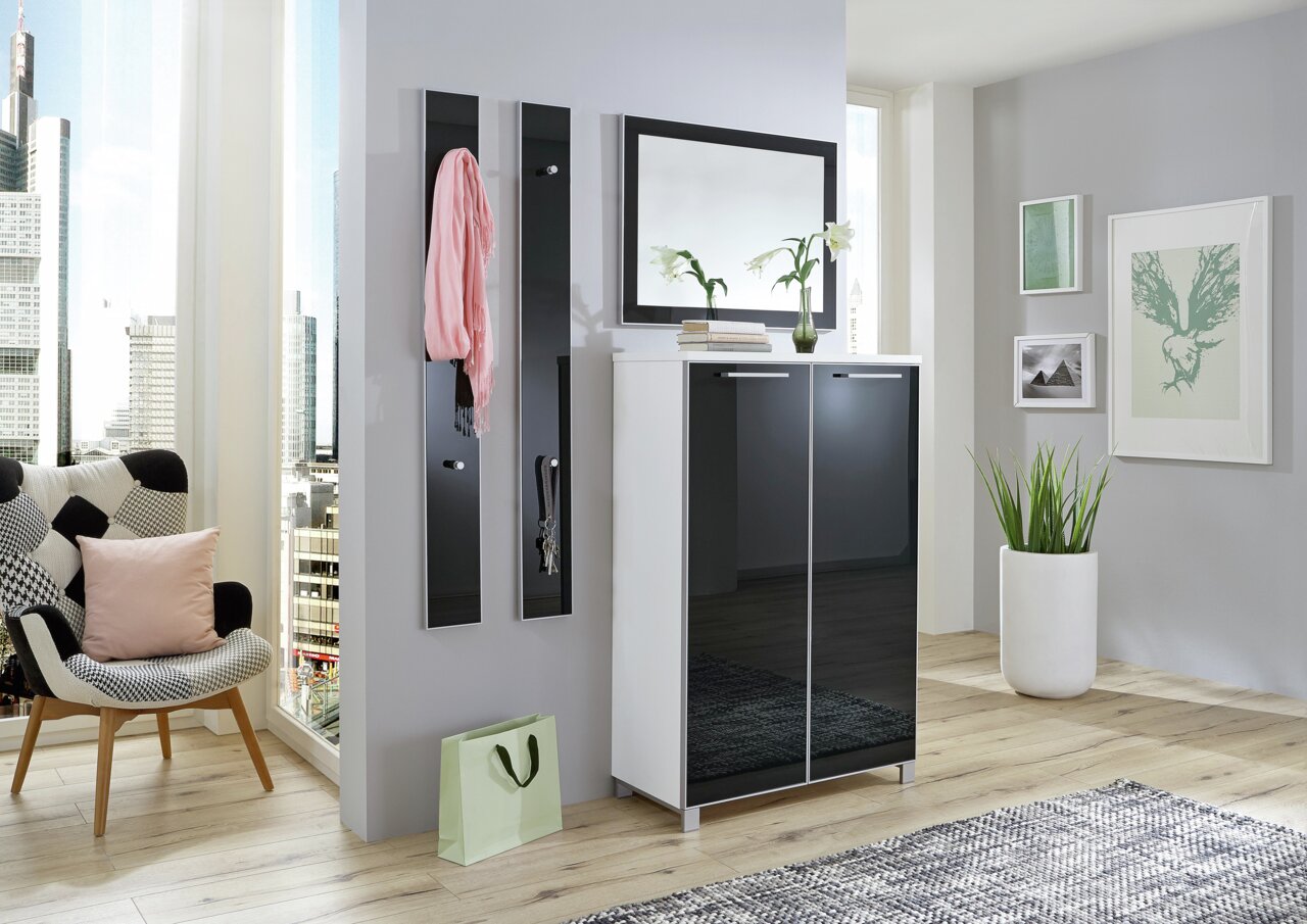 Moderner Eingangsbereich mit einem stilvollen Spiegel über einem weißen Schrank mit schwarzen Türen, dekoriert mit Pflanzen und Büchern, in einer hellen, urbanen Wohnung.