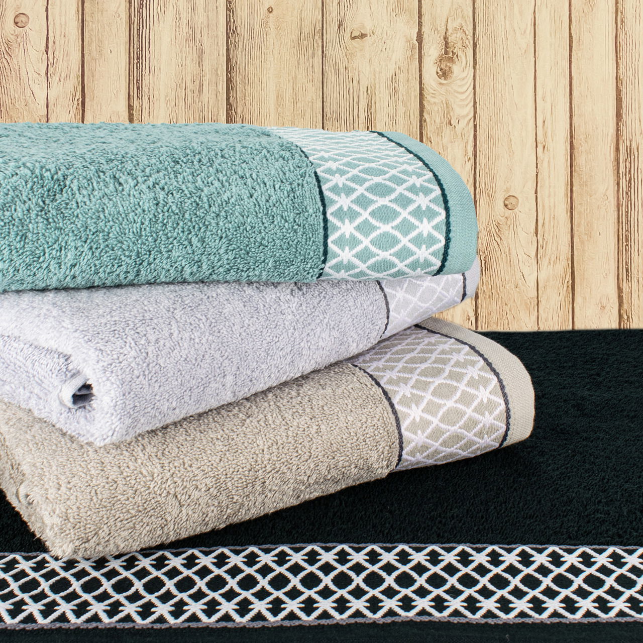 Frottana Handtuchset Cashmere ORIENTAL ORNAMENTS Drei gefaltete Handtücher in verschiedenen Farben mit orientalischen Mustern, gestapelt vor einer Holzwand. Perspektive von vorne.