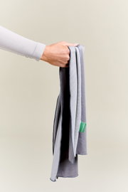 Een hand houdt een grijze sporthanddoek met een groen label vast, gezien vanuit een zijaanzicht.