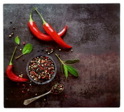 Herdabdeckplatte mit roten Chilischoten, Pfefferkörnern und grünen Blättern aus der Vogelperspektive