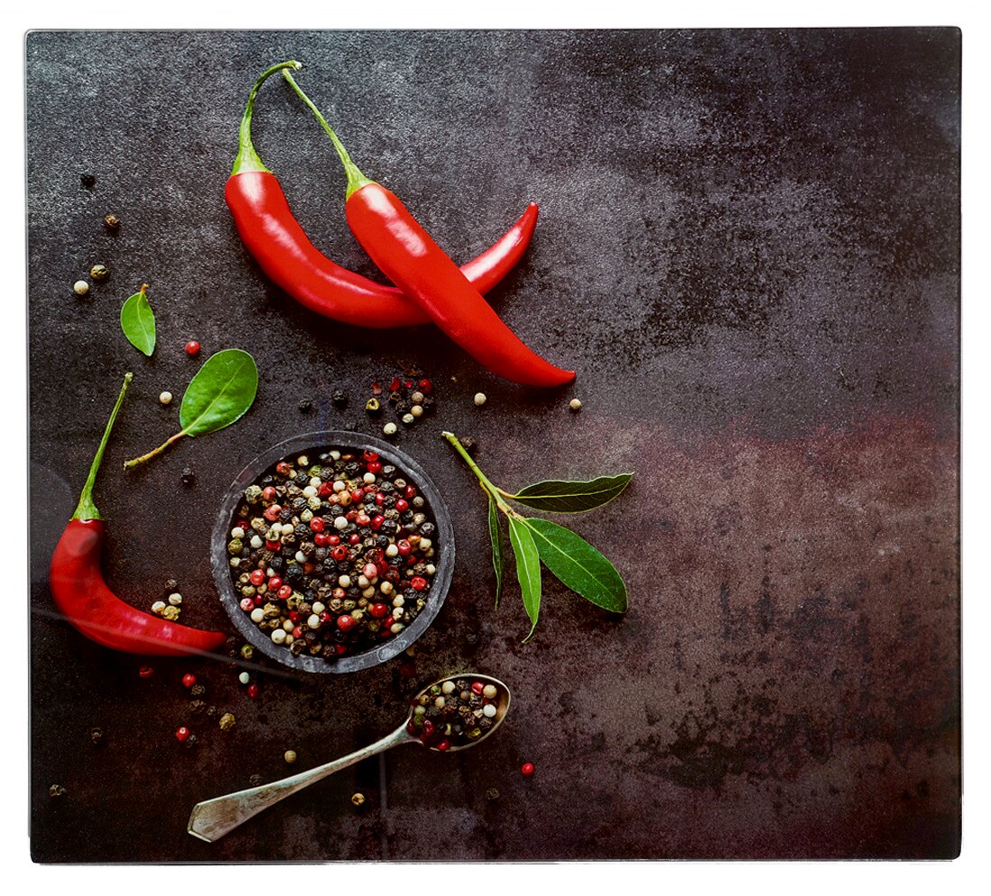 Herdabdeckplatte mit roten Chilischoten, Pfefferkörnern und grünen Blättern aus der Vogelperspektive
