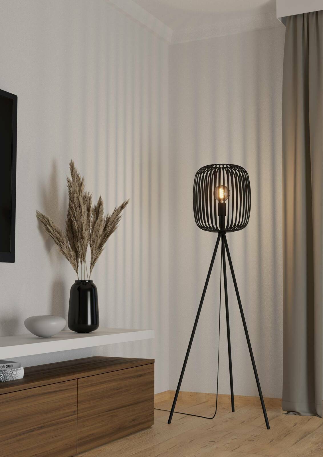 Moderne Stehleuchte ROMAZZINA mit schwarzem, dreibeinigem Gestell und offenem Lampenschirm in einem stilvollen Wohnzimmer, seitliche Perspektive.