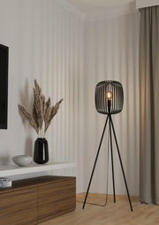 Moderne Stehleuchte ROMAZZINA mit schwarzem, dreibeinigem Gestell und offenem Lampenschirm in einem stilvollen Wohnzimmer, seitliche Perspektive.