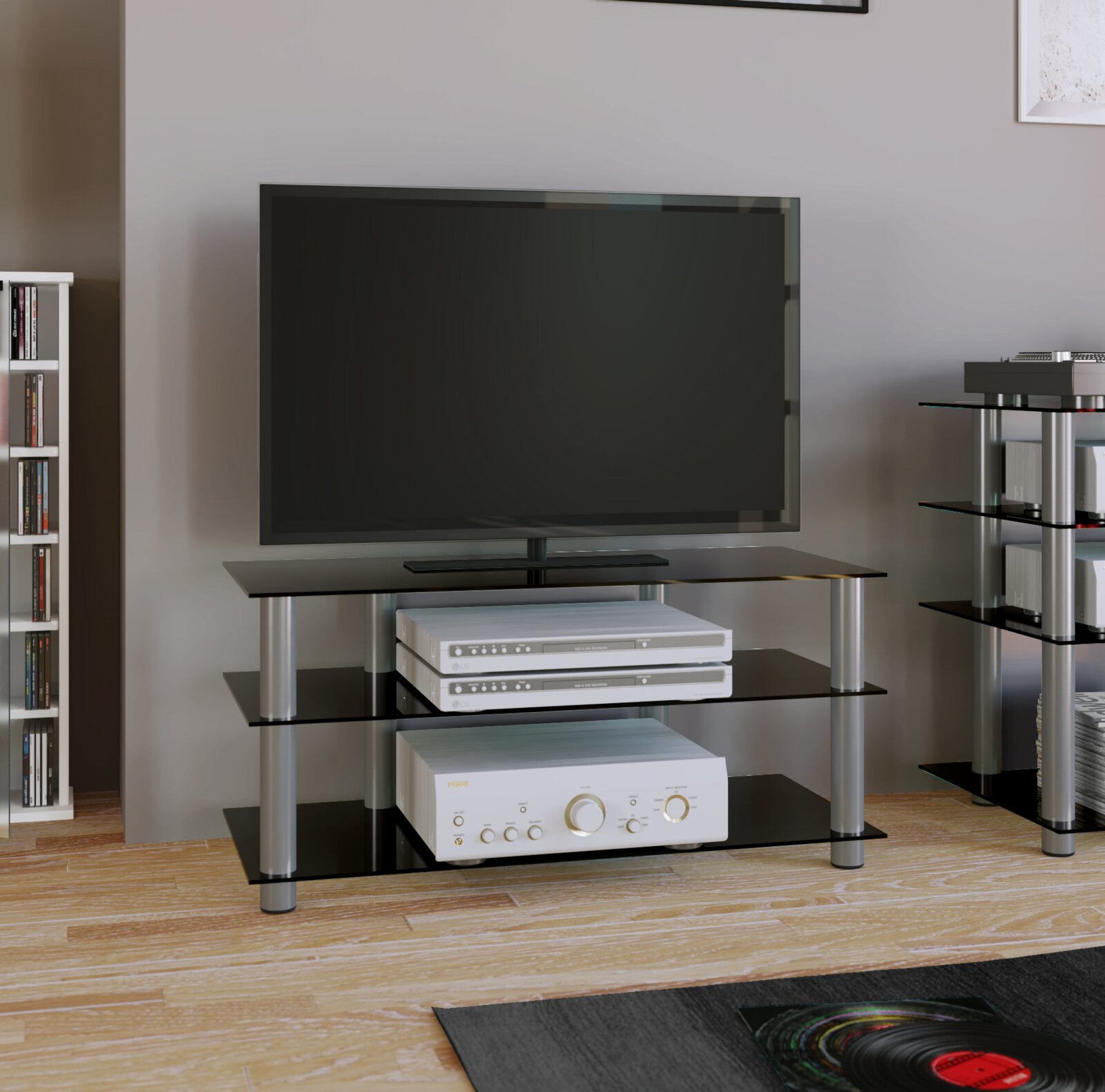 Modernes TV-HiFi-Rack mit schwarzen Glasböden und silbernen Metallstützen, darauf ein Flachbildfernseher und Audio-Komponenten frontale Perspektive auf das Möbel im Wohnzimmer.