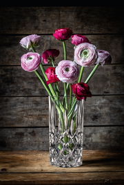 Kristallvase mit Blumenstrauß, frontal fotografiert vor rustikalem Holzhintergrund.