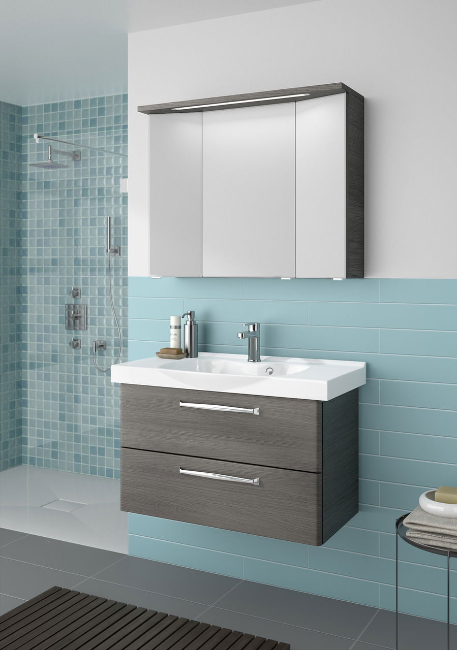 Moderner Badblock mit grauen Schubladen und weißem Waschbecken, frontal betrachtet, vor einer Wand mit blauen Fliesen.