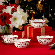 Vier festliche Schalen mit weihnachtlichen Motiven, präsentiert auf einem Tisch mit rotem Tuch, im Hintergrund ein geschmückter Weihnachtsbaum und ein Blumenarrangement. Perspektive: seitlich von vorne.