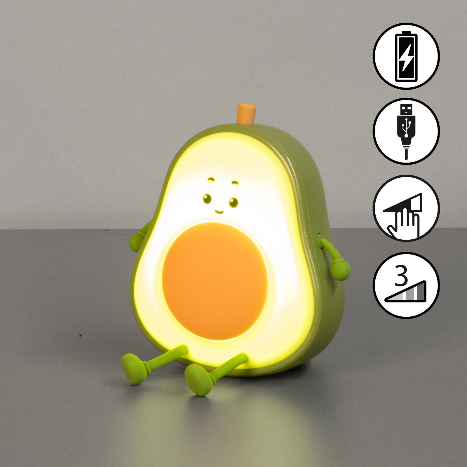 Niedliches Akku-Nachtlicht in Form einer Avocado mit Gesicht, das auf einem Tisch sitzt. Vorderansicht mit leuchtendem Kern und kleinen Armen und Beinen.