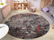 Runder Designer Teppich in einem modernen Wohnzimmer, mit abstraktem Muster in Grau- und Rottönen, aus der Vogelperspektive betrachtet.