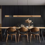Moderne Pendelleuchte PURE-MOTO-RISE über einem Esstisch, aus Holz und Metall, in einem stilvollen Esszimmer mit dunklen Wänden, seitliche Perspektive.